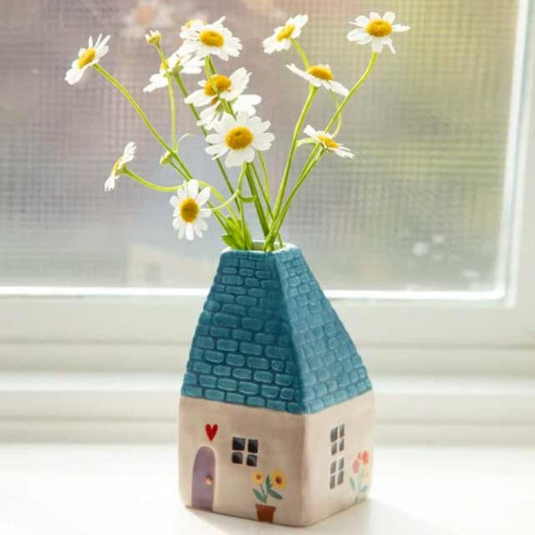 Her er den sødeste vase nogensinde i form af et lille hus. Den har et turkisfarvet tag og endda et lille vindue og en dør dekoreret med blomster og hjerter hele vejen rundt! Stil denne smukke keramikvase i vinduekarmen eller på en lille hylde, og glem ikke at sætte en lille blomst i den.