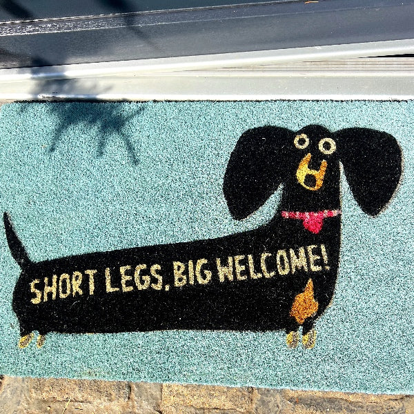 Gulvmåtte med en sød gravhund og citatet: Short legs, big welcome. Måtten skaber personlighed og humor allerede inden man træder indenfor - Find interiør der står ud af mængden og giver smil på læben online hos RAUMTRAUM.dk