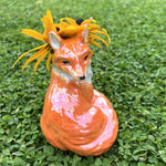 Denne dekorative rævevase er fuld af charme og personlighed. Lavet i dolomit i flotte farver og blank glasur. Den er ideel til en lille buket blomster, men fungerer også som en skulpturel skulptur i sig selv.
Den spreder smil uanset om den står på hylden i stuen, på skrivebordet eller som hyggelig dekoration på børneværelset.